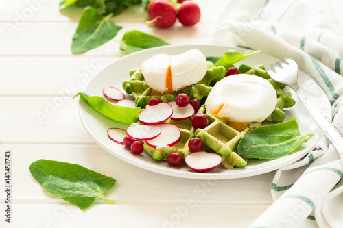 Healthy breakfast: spinach waffles with radish slices and poached eggs on white wooden table. Selective focus