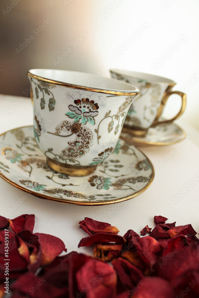 Fototapeta premium Tea cup and saucer on white table with rose petals