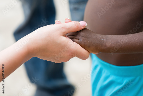Holding hands.Caucasian woman's hand holding African black little girl's hand.Unrecognizable people, close up
