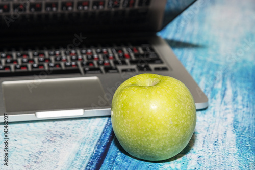 Open notebook with an big green apple on the blue wooden table
