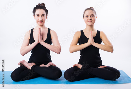 Two women doing yoga and meditating in lotus position isolated on white background.