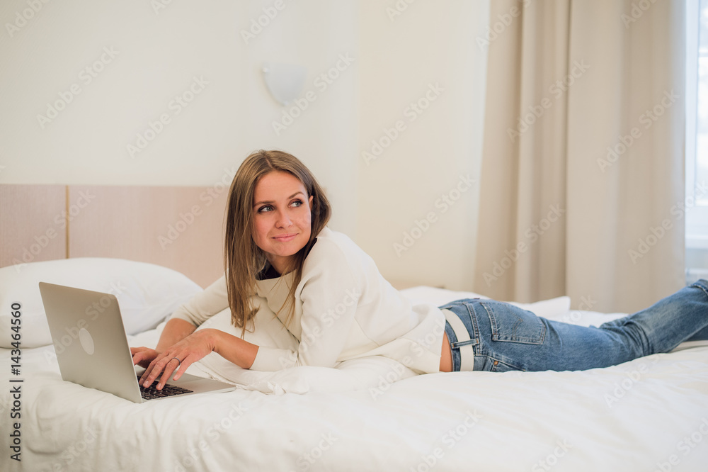 A cute young woman smiling excitedly at her laptop screen. She is relaxing in bed. A cute young woman smiling excitedly at her laptop screen. She is relaxing in bed.
