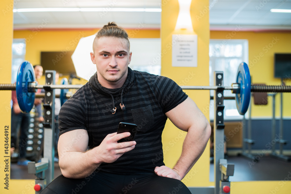 Young handsome man using phone while having exercise break in gym. Young handsome man using phone while having exercise break in gym.
