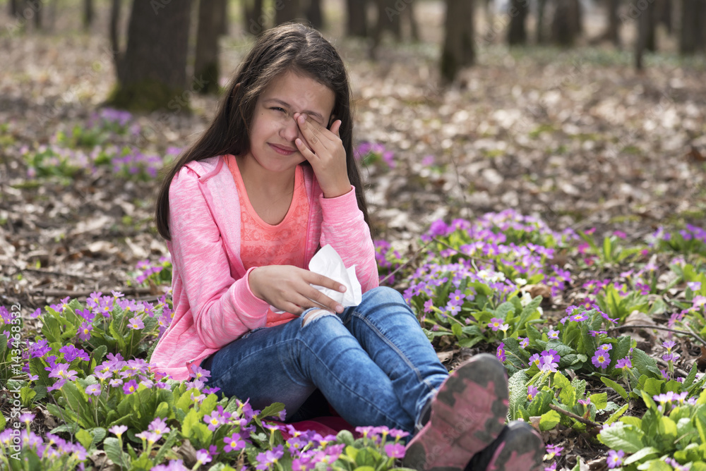 Girl sitting among primroses and rubbing her eyes
