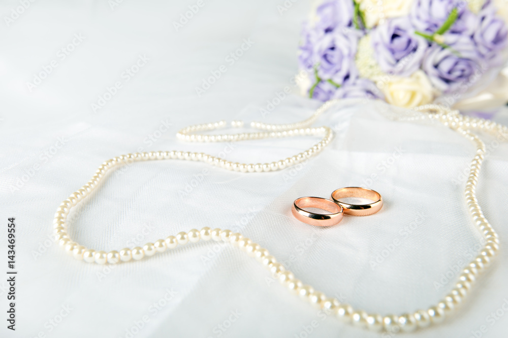 Gold wedding rings lie on a wedding dress. Against the background of the necklace of pearls Gold wedding rings lie on a wedding dress. Against the background of the necklace of pearls