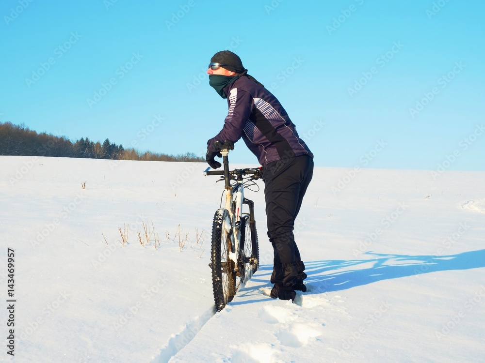 Biker pushing mountain bike on snow drift. Freeze sunny winter weather. Biker is pushing bike in deep snow