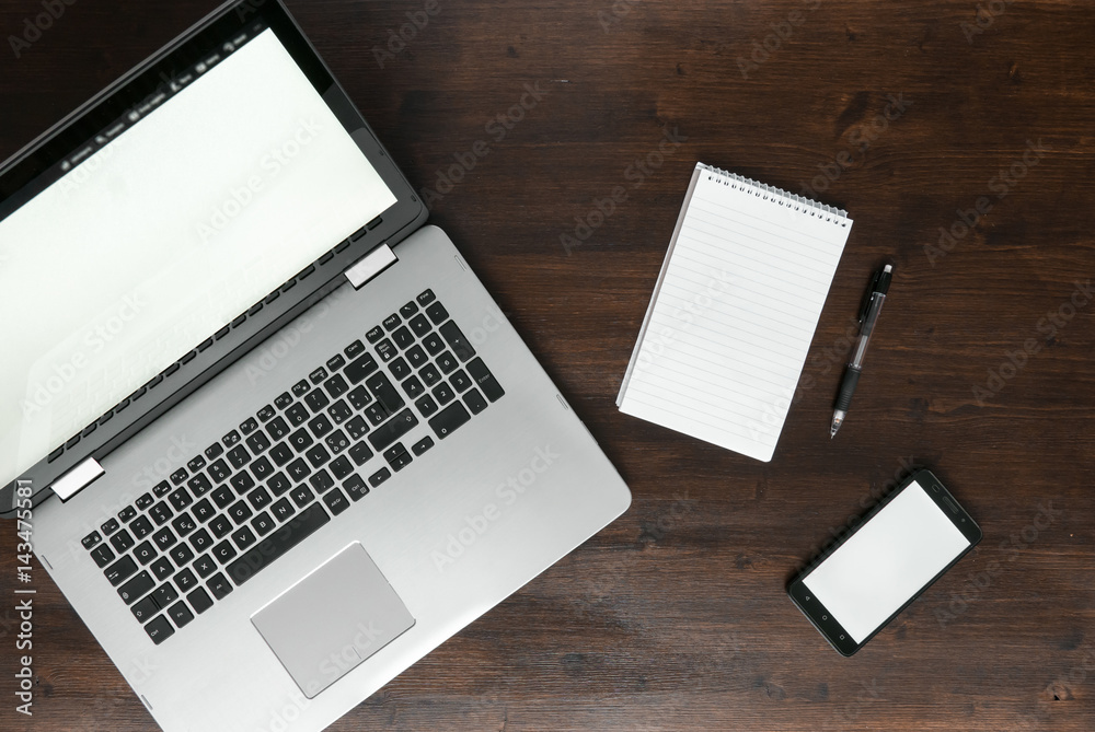 Top view of laptop smartphone and notepad on dark brown wooden desk, workspace concept Top view of laptop smartphone and notepad on dark brown wooden desk, workspace concept