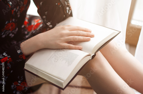 the girl sits at the window and reading a book. out the window the sun is shining