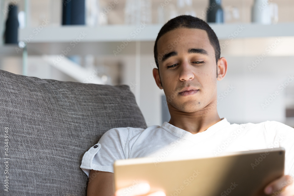 Man lying on sofa and looking at tablet