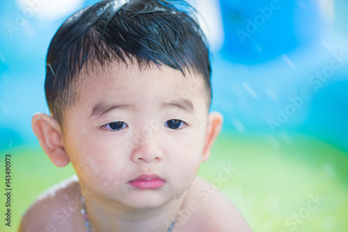 Sad Asian kid playing alone in inflatable baby pool.