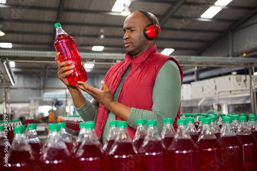 Male worker wearing protective earwear while inspecting bottle photo