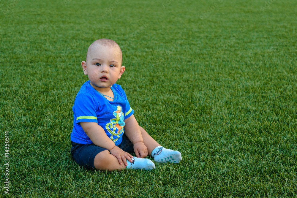 the little boy sits on a green grass of the football field. the little boy sits on a green grass of the football field.