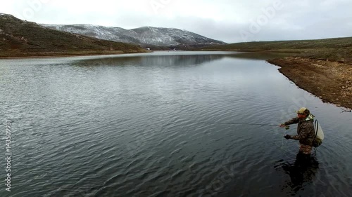 Fly fisherman casting line as he stands in a lake photo