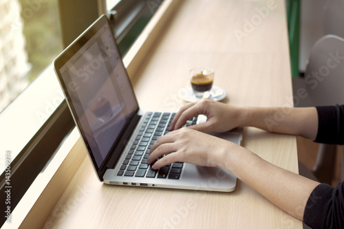 woman‘s hands typing on notebook keyboard with coffee on wooden desk