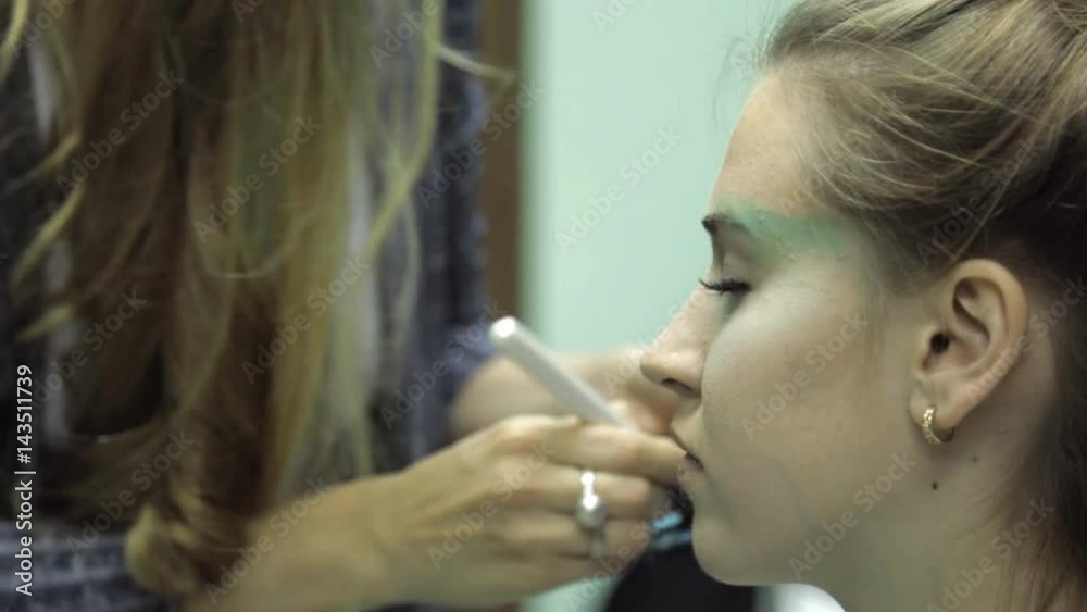 Professional makeup on a model face closeup a visage course. Young makeup designer teaches to applying eye shades on a model profile using eyeshadow palette. Green color on an eye brow ridge and Professional makeup on a model face closeup a visage course. Young makeup designer teaches to applying eye shades on a model profile using eyeshadow palette. Green color on an eye brow ridge and
