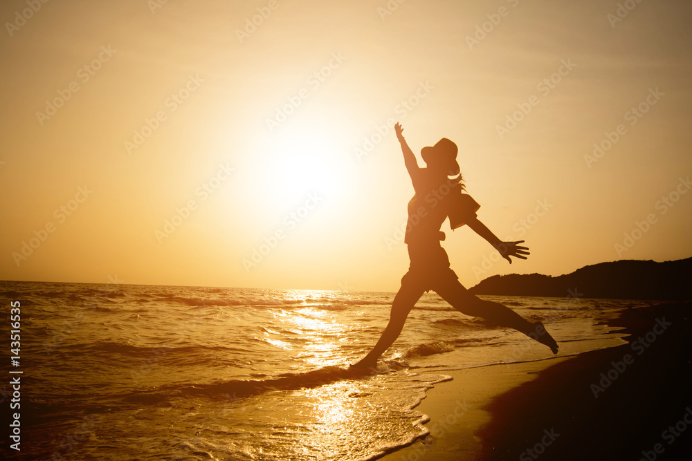 silhouette of happy woman stand on sand of the sea and show hand in to sky with sunset.