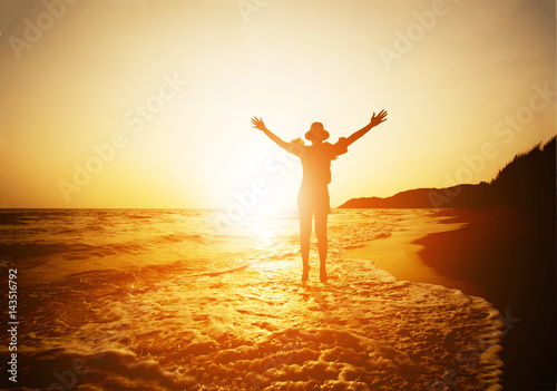 silhouette of happy woman stand on sand of the sea and show hand in to sky with sunset.