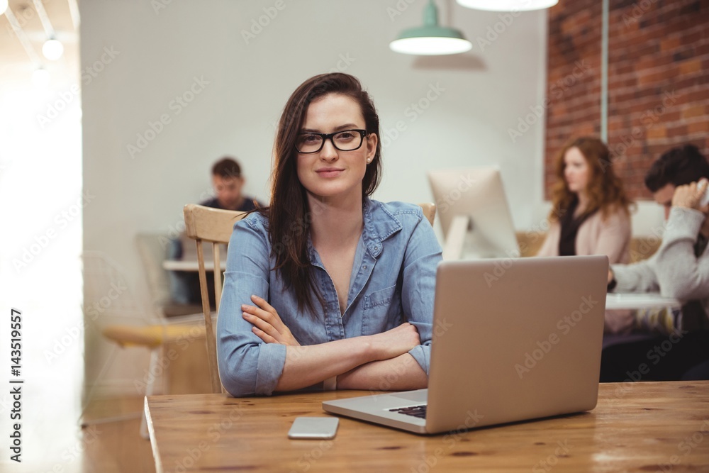 Female executive sitting with arms crossed at desk