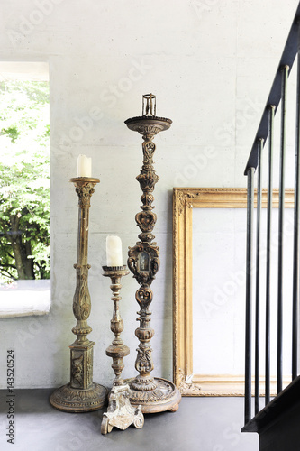 Large antique church candle holder with gold leaf frame and aluminum staircase on a concrete wall and window on the garden photo