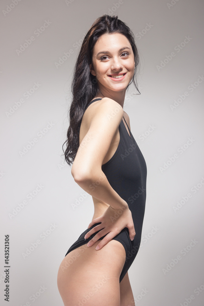 one young woman, standing swimmer swimsuit, looking sideways glance smiling