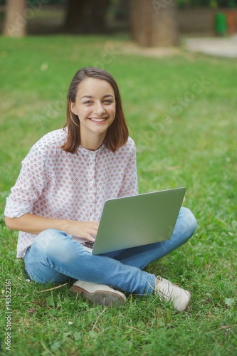 Young woman with laptop sitting on green grass