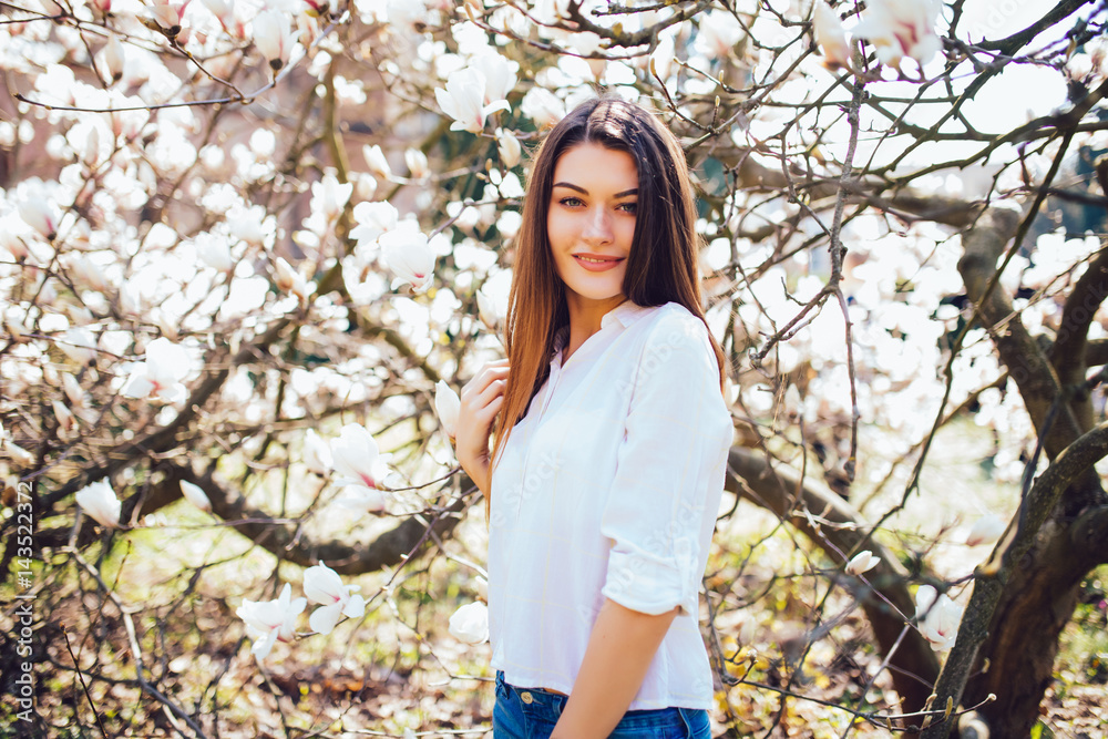 Spring portrait of happy woman standing on background Magnolia blossoming flowers. Spring season