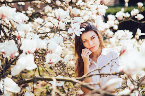 Beautiful woman portrait in blossoming magnolia tree flowers in a sunny day of spring.