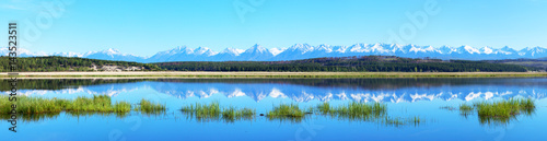 Panorama of the spring flood of the river. Snow-capped peaks of the Eastern Sayan Mountains are reflected in the blue water of the river