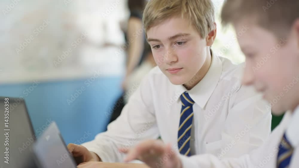 2 young boys working on computers, helping each other in school lesson