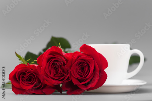 Red roses with a coffee cup of white color on a gray background