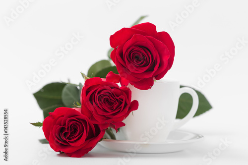 Red roses with coffee cup of white color on a white background.