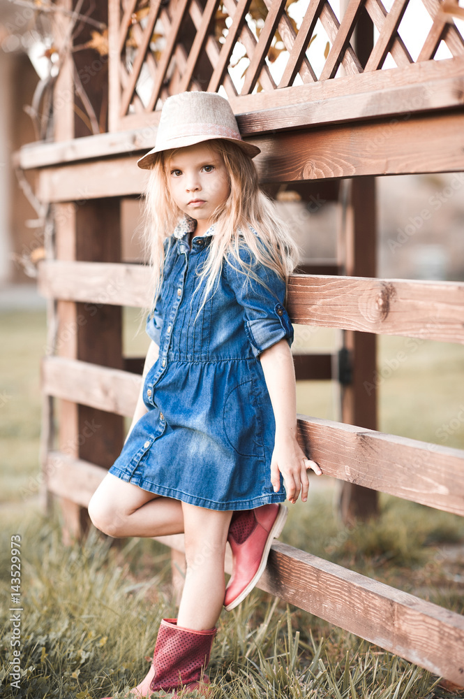Stylish baby girl 4-5 year old wearing stylish denim dress in park. Looking at camera. Childhood.