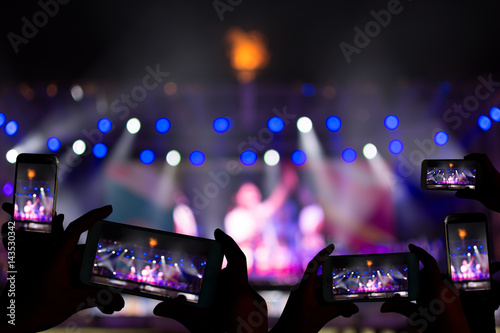 Silhouette of hands using camera phone to take pictures and videos at live concert.