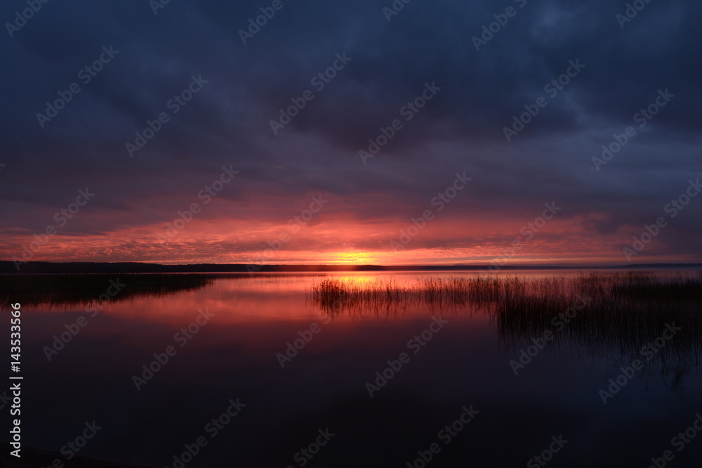 Gloomy sunset in the cloudy sky above the surface of the lake water