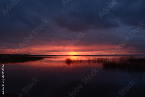 Gloomy sunset in the cloudy sky above the surface of the lake water