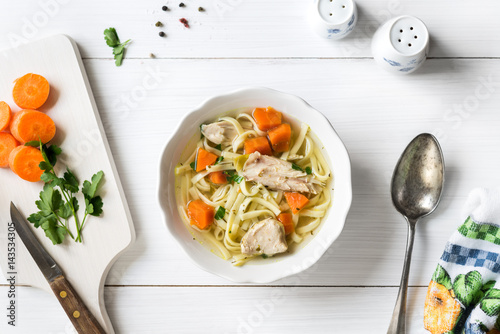 Top view of chicken soup with pasta, carrot and parsley on white table
