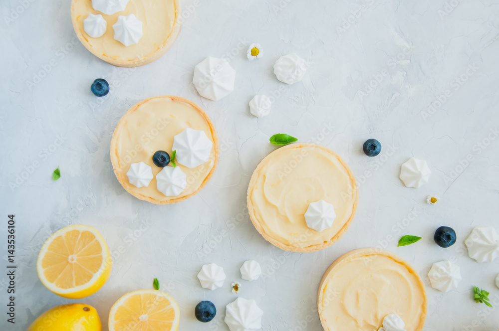 Individual lemon curd tarts with blueberry jam meringue and basil leaves on a white stone background. Flat lay and copy space. Individual lemon curd tarts with blueberry jam meringue and basil leaves on a white stone background. Flat lay and copy space.