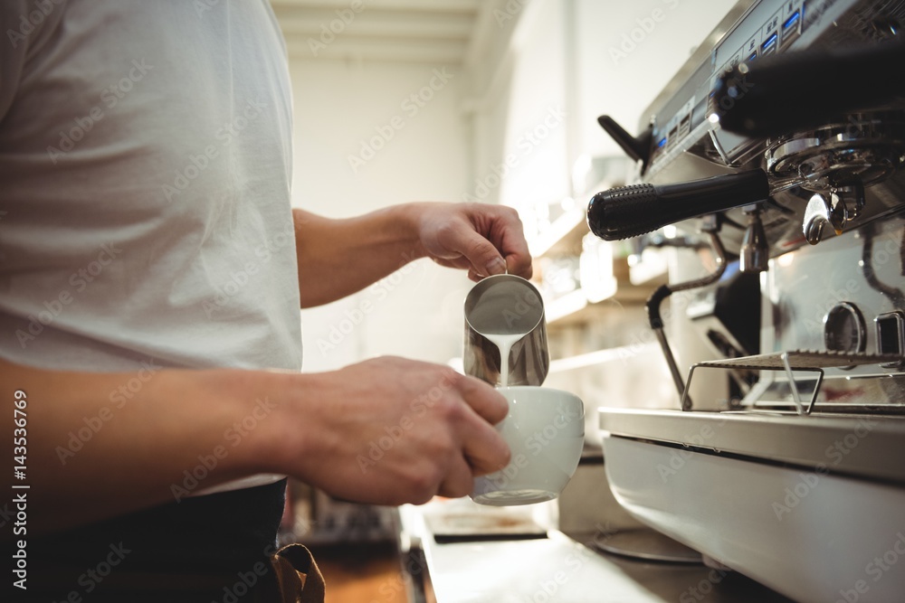 Male barista pouring milk into coffee cup at cafe Male barista pouring milk into coffee cup at cafe