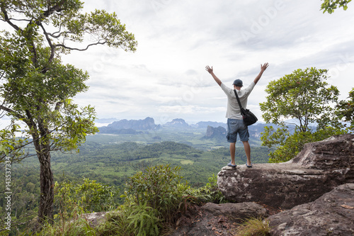 Traveler man standing on big stone holding his hand up and see landscape view at Dragon Crest mountain  popular landmark travel adventure in krabi thailand.