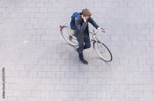 Young man with backpack wheeling vintage bike in city talking on phone from above