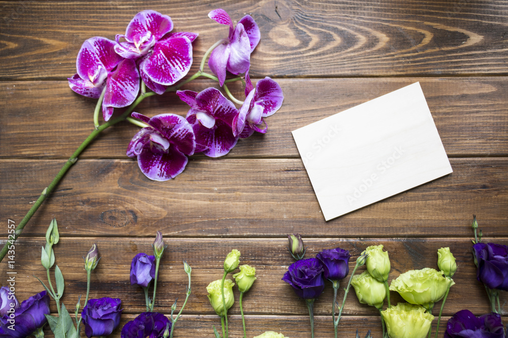 Stylish floral background of violet eustoma flowers, and orchid on the wooden background. Blank greeting card with flowers