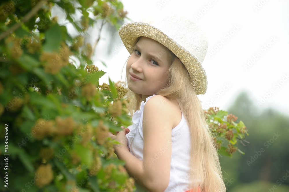 Fototapeta premium Little blonde girl wearing a hat in the garden.