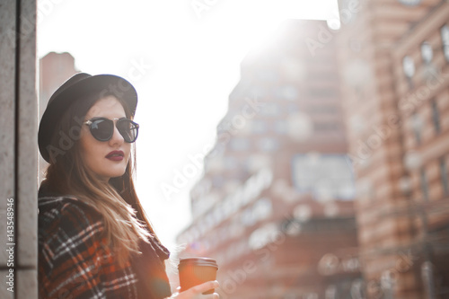 Beautiful young girl in a hat and holds a cup of coffee on urban background