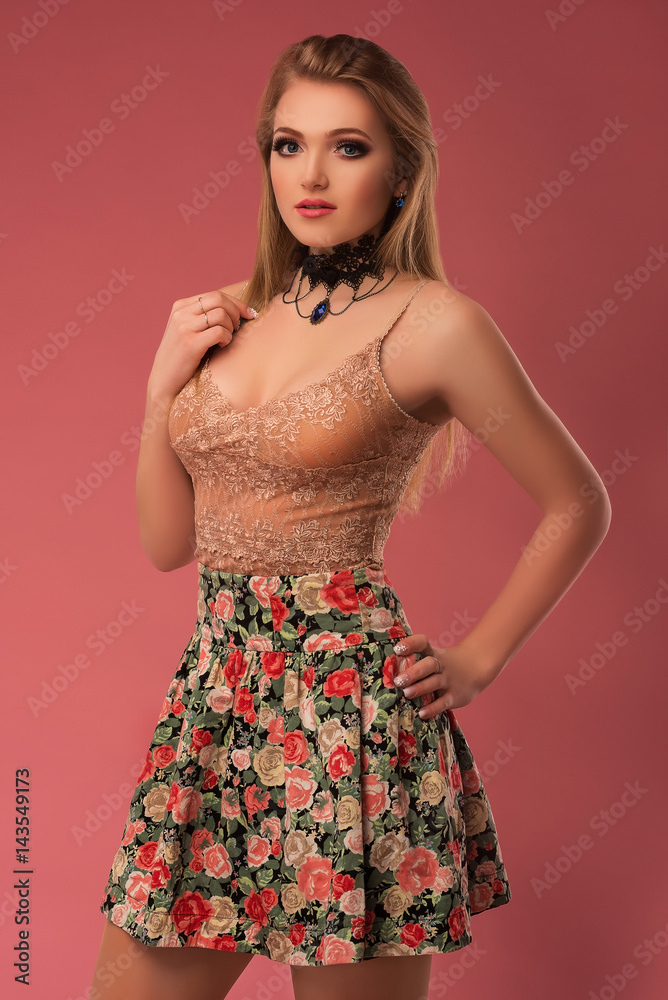 Fashion photo of a beautiful young woman in a pretty clothes with flowers posing on the pink background. Fashion photo
