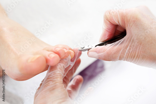Pedicure leczniczy. Kosmetyczka wycina cążkami skórki przy paznokciach i wykonuje profesjonalny pedicure.