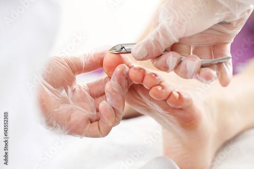 Podologia, wycinanie skórek. Kosmetyczka wycina cążkami skórki przy paznokciach i wykonuje profesjonalny pedicure.
