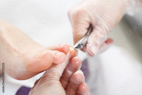 Profesjonalny pedicure w gabinecie kosmetycznym. Kosmetyczka wycina cążkami skórki przy paznokciach i wykonuje profesjonalny pedicure.