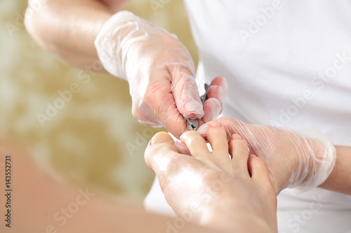 Kosmetyczka wycina cążkami skórki przy paznokciach i wykonuje profesjonalny pedicure.