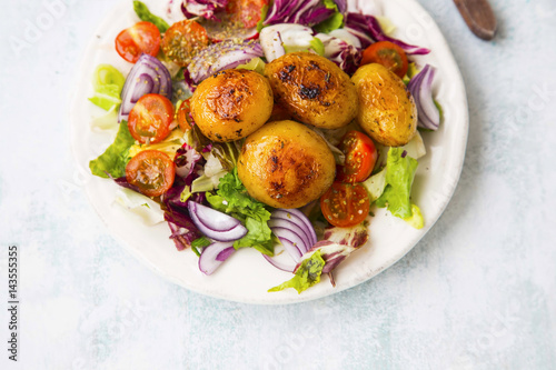 Spiced roasted potatoes with fresh organic vegetables salad with tomatoes, lettuce, onion