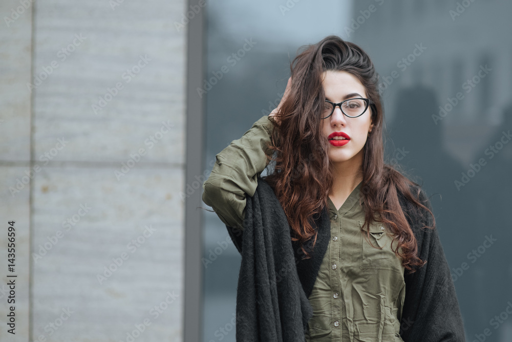 Fashion consept: beatiful young girl with long hair, glasses, red lips standing near modern wall wearing in green suit and grey jeans. She wanted talking on phone close eyes Fashion consept: beatiful young girl with long hair, glasses, red lips standing near modern wall wearing in green suit and grey jeans. She wanted talking on phone close eyes